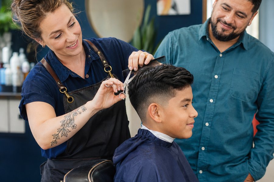 Barber giving a child a haircut while his dad watches